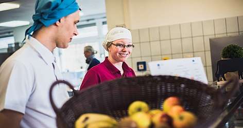 Zwei Küchenmitarbeiter mit Obstkorb in einer modernen Küche.